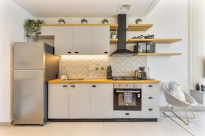 Eine moderne Küche mit Backofen, einem Edelstahl-Kühlschrank und Holzregalen darüber.