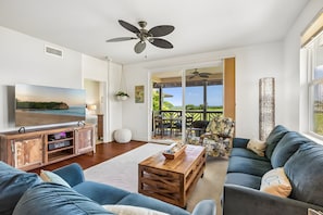 A spacious living room with a television, a ceiling fan, and a view of the outdoors. - Poipu, Pili Mai, Spacious 6 BR, Ocean View, Sleeps 16 (Koloa)