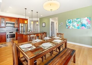 Una cocina moderna con electrodomésticos de acero inoxidable, una mesa de comedor de madera para cuatro comensales y una lámpara colgante grande.