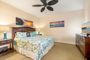 A bedroom with a bed, nightstands, a dresser, a ceiling fan, and two wall-mounted paintings. - Poipu, Pili Mai, Spacious 6 BR, Ocean View, Sleeps 16 (Koloa)
