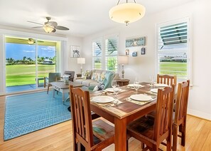 Comedor con mesa de madera para seis comensales, ventilador de techo y vistas a un campo de golf a través de amplias ventanas.