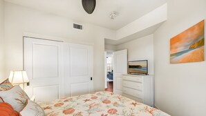 A bedroom with a bed, a dresser, a television, and a painting on the wall. - Ocean View 5BR, 2 Condos for 14 in Koloa! (Koloa)