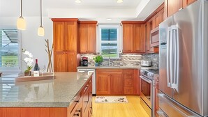 A modern kitchen with wooden cabinets, stainless steel appliances, and a large island. - Ocean View 5BR, 2 Condos for 14 in Koloa! (Koloa)