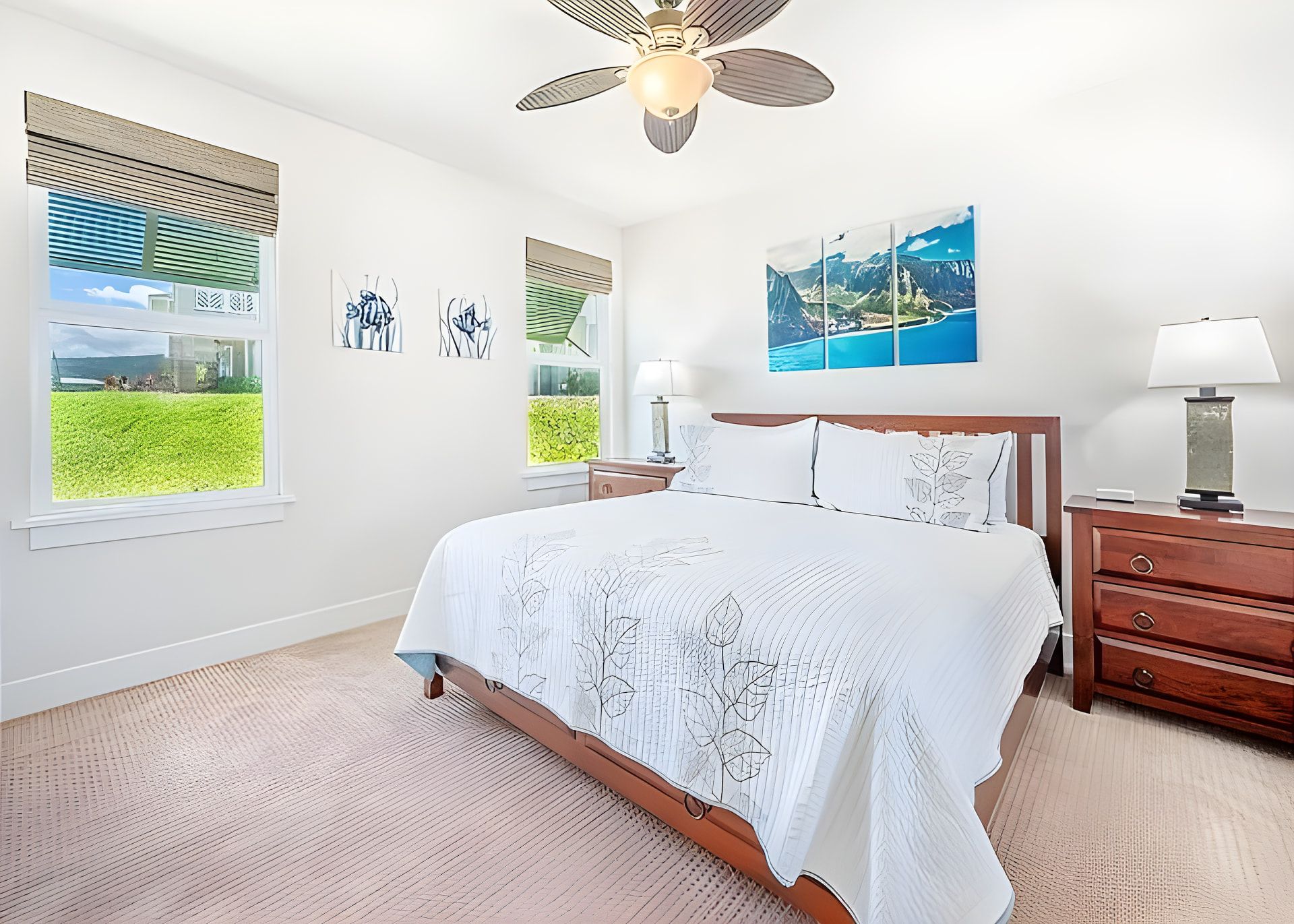 A bedroom with a bed, a nightstand, a lamp, a ceiling fan, and artwork on the walls.