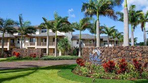 A hotel with multiple-story buildings, a stone wall with a sign, and tropical landscaping. - Ocean View 6BR, 2 Condos for 16 in Koloa! (Koloa)