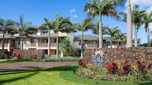Un hôtel composé de plusieurs bâtiments à étages, doté d’un mur en pierre avec une enseigne et agrémenté d’un aménagement paysager de style tropical.