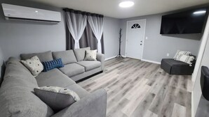 Un salon moderne avec un canapé d’angle gris, un téléviseur à écran plat fixé au mur et un plancher en bois.