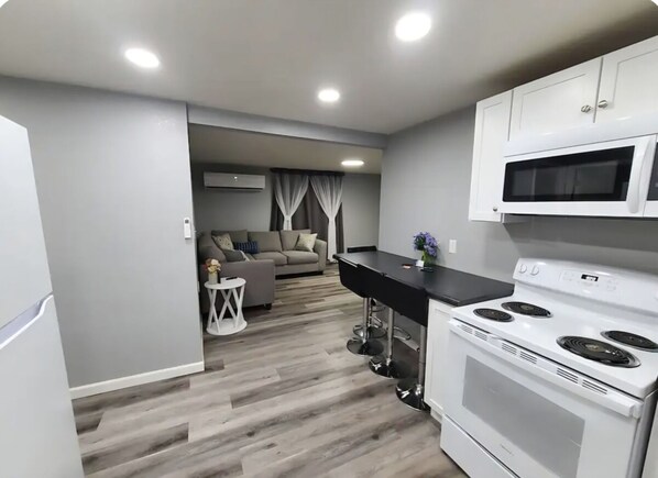 Cozinha compacta com eletrodomésticos brancos, área de refeições com sofá e pequena mesa lateral.
