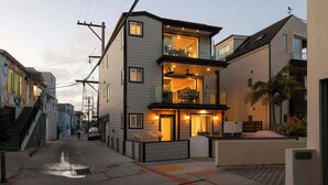 Un edificio moderno de dos pisos con un balcón, entrada visible y un pequeño espacio al aire libre para sentarse.