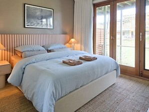 A bedroom with a large bed, two bedside tables, a window with curtains, and a view of the outside.