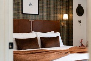 Ein Hotelzimmer mit karierter Tapete, einem gerahmten Bild an der Wand, einem Kopfteil, einer Nachttischlampe und einem Bett mit braunen Bettwaren.