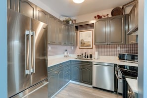 Eine moderne Küche mit Edelstahlgeräten, grauen Schränken und einer karierten Spritzschutzwand.
