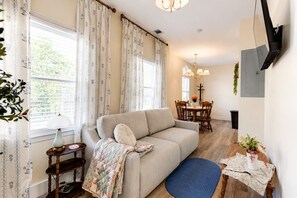Un salon comprenant un canapé, une table à manger et des chaises, une lampe et un téléviseur fixé au mur.