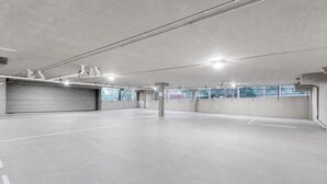Un amplio garaje con pisos y paredes de concreto, iluminación en el techo y una puerta cerrada.