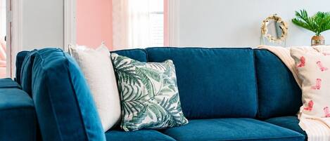 Un sofá seccional color turquesa con un cojín estampado, una manta blanca y una pequeña planta en maceta.