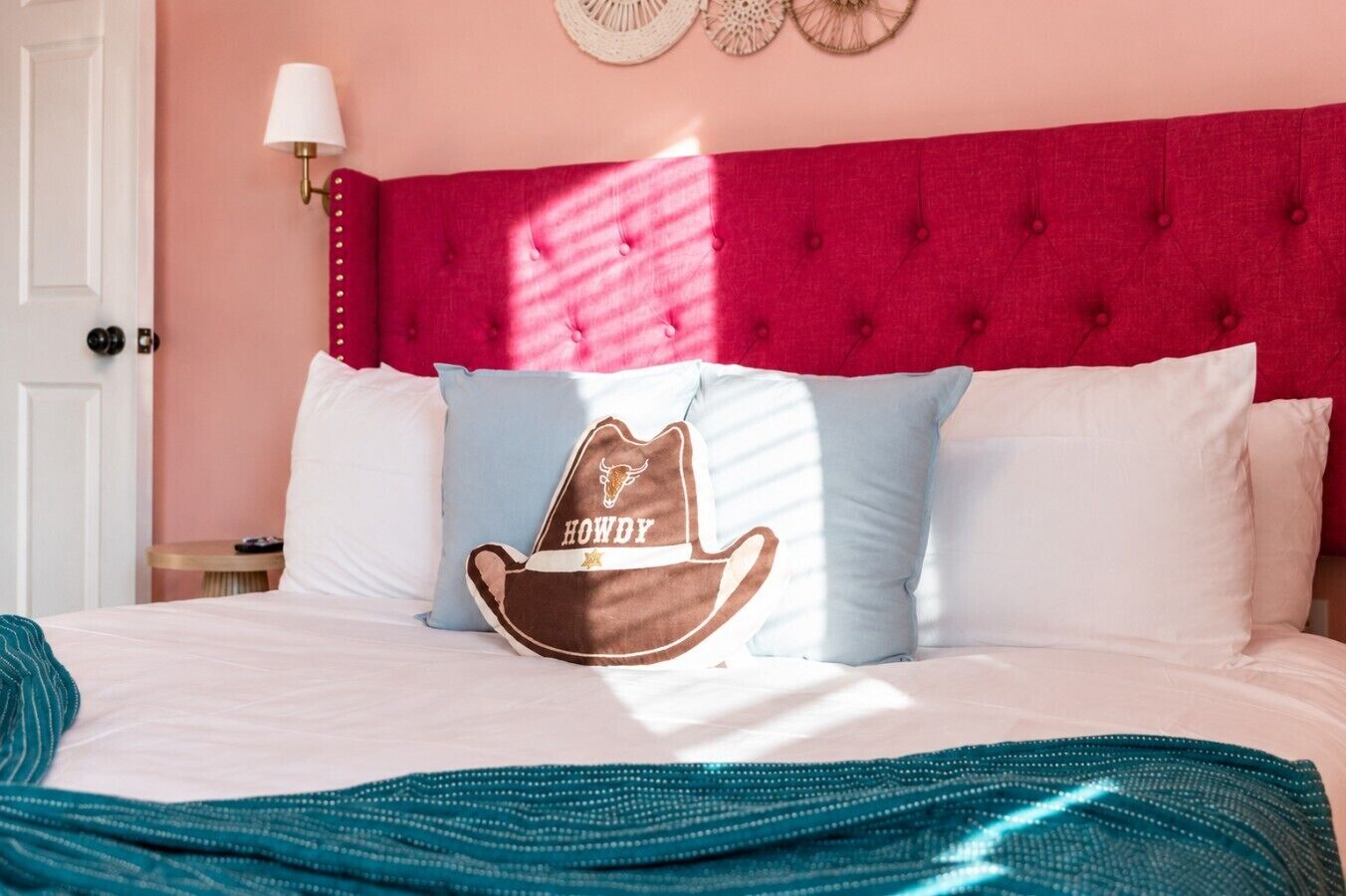 Ein Bett mit dunkelrotem Kopfteil, einem Kopfkissen mit Cowboyhut-Motiv und einer türkisblauen Decke.