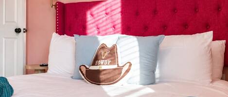 Ein Bett mit dunkelrotem Kopfteil, einem Kopfkissen mit Cowboyhut-Motiv und einer türkisblauen Decke.