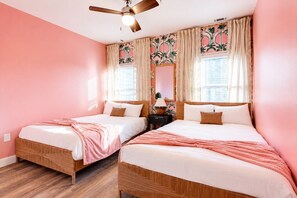 Ein Zimmer mit zwei Betten, einem Deckenventilator und einem Fenster mit Vorhängen.
