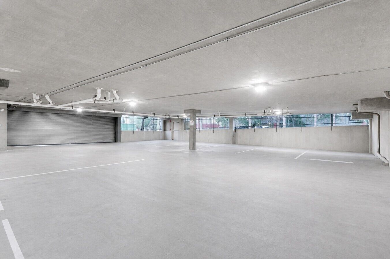 Eine geräumige Tiefgarage mit Betonböden und -wänden, Deckenbeleuchtung und einer geschlossenen Garagentür.