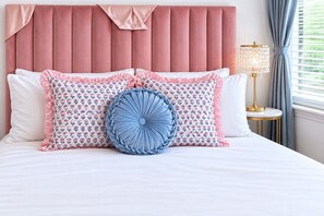 Ein Bett mit einem rosa Kopfstück, Kissen mit Blumenmuster und einem blauen Zierkissen.