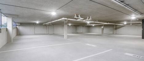 Eine leere Parkgarage mit Betonböden und -wänden, einer weißen Deckeninstallation und einigen sichtbaren Säulen.