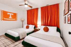 A hotel room with two beds, orange curtains, a ceiling fan, a plaid carpet, and a Tennessee flag. - Game Day Getaway | Vols-Themed Stay Near Vanderbilt (Nashville)