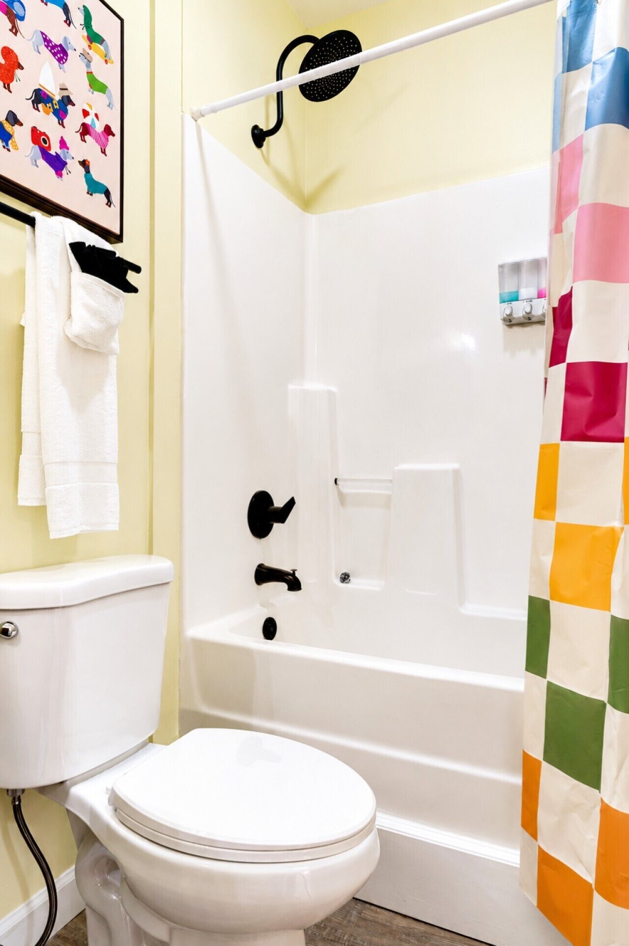 A bathroom with a white toilet, a shower with a black showerhead, and a colorful curtain.