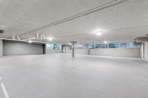 Eine geräumige Tiefgarage mit Betonböden und -wänden, Deckenbeleuchtung und einer geschlossenen Garagentür.