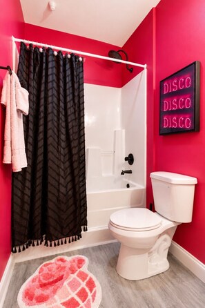 Ein Badezimmer mit einer weißen Badewanne, einer weißen Toilette, einem schwarzen Duschvorhang und einer roten Wand mit einem Neonzeichen.