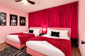 Ein Schlafzimmer mit zwei Betten, roten Vorhängen, einem zebra-gemusterten Teppich und Wandkunst mit einer Discokugel.