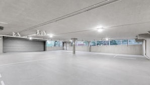 En rummelig parkeringskælder med beton gulve og vægge, belysning fra oven og en lukket garageport.