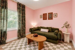A room with a checkered floor, a green sofa, a wooden coffee table, and floral curtains. - Relaxing Bohemian Retreat | Walk to Sportsplex (Nashville)
