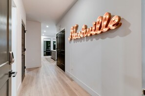 A hallway with a modern interior design, a wall-mounted illuminated sign reading 'Nathalie,' and a door leading to a room. - Two Kings on Top Floor w/ Pool & Patio (Nashville)