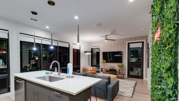 Een moderne keuken met een centraal eiland, een zithoek met een bank en een woonkamer met een televisie.