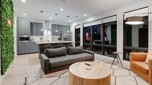 Een moderne keuken met grijze kastjes, een centraal eiland en een zithoek met een bank en salontafel.