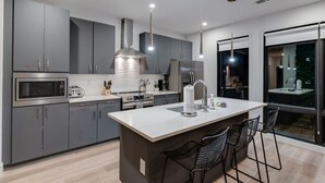 Een moderne keuken met grijze kastjes, een centraal eiland, roestvrijstalen apparatuur en een groot raam.