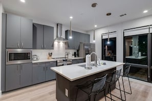A modern kitchen with grey cabinets, a central island, stainless steel appliances, and a large window. - Two Kings on Top Floor w/ Pool & Patio (Nashville)