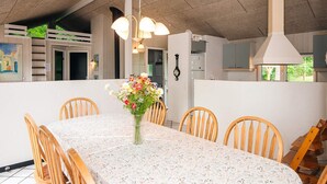 A dining area with a table set for six, surrounded by wooden chairs, a vase of flowers, and pendant lighting. - 4 Star Holiday Home in Glesborg (Glesborg)
