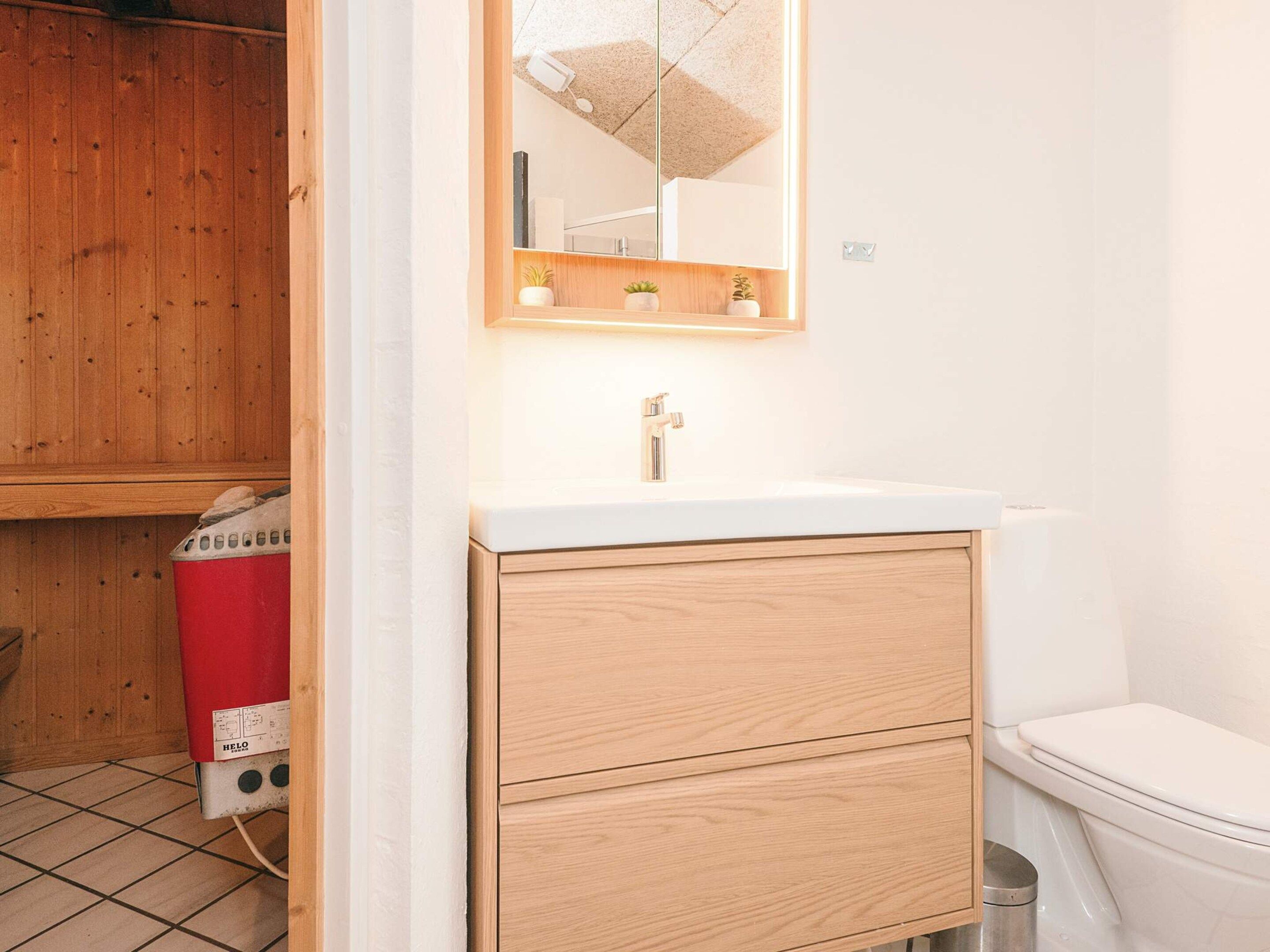 A bathroom with a white sink, wooden cabinet, and a mirror above it.