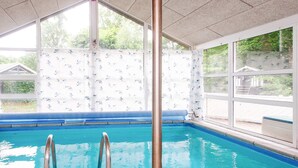 An indoor swimming pool with clear glass walls, a tiled floor, and a metal pole in the foreground. - 4 Star Holiday Home in Glesborg (Glesborg)