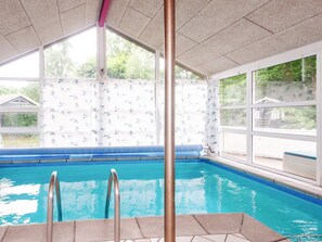 An indoor swimming pool with clear glass walls, a tiled floor, and a metal pole in the foreground. - 4 Star Holiday Home in Glesborg (Glesborg)