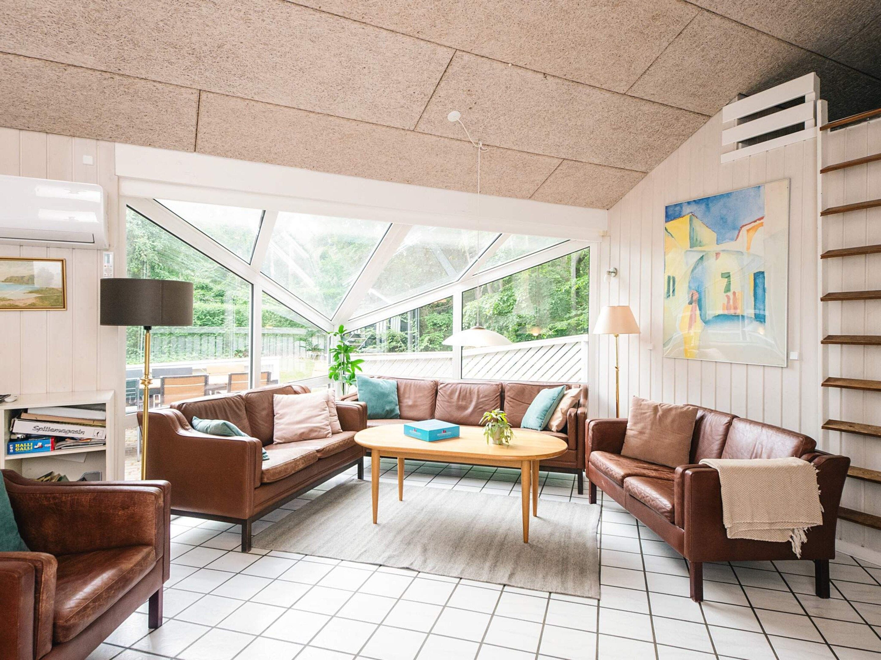 A spacious living room with a large window, a brown leather sofa set, a wooden coffee table, and a painting on the wall.