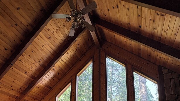 A spacious living area with a high ceiling, large windows, a sofa, a coffee table, and a stone wall. - Enjoy a serene 3 bedroom cabin located in Blue Lake Springs, Arnold. (Arnold)