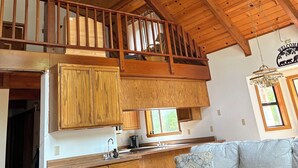 A loft-style room with a wooden ceiling, a staircase, a kitchen area, and a sofa. - Enjoy a serene 3 bedroom cabin located in Blue Lake Springs, Arnold. (Arnold)