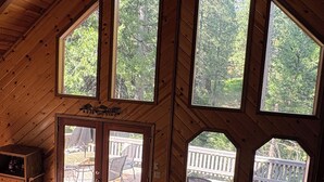 A cabin interior with a loft-style ceiling, large windows, a sofa, a coffee table, and a door leading to an outdoor deck. - Enjoy a serene 3 bedroom cabin located in Blue Lake Springs, Arnold. (Arnold)