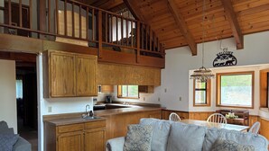 A spacious loft-style living area with a kitchen, a dining table, and a sofa with patterned cushions. - Enjoy a serene 3 bedroom cabin located in Blue Lake Springs, Arnold. (Arnold)