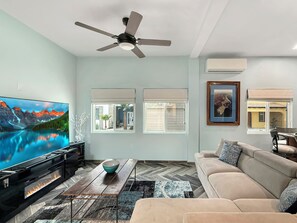 A living room with a flat-screen TV, a ceiling fan, a fireplace, a sofa, and a dining area. - Cozy 1-bedroom, sleeps 4, AC, Electric Vehicle Charger, Courtyard, BBQ grill (Bahía la Choya)