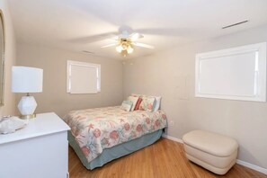 A bedroom with a bed, a desk, a chair, a ceiling fan, and a window.
