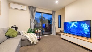 A modern living room with a grey sofa, a flat-screen TV, and a sliding glass door leading to a balcony.