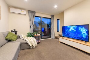A modern living room with a grey sofa, a flat-screen TV, and a sliding glass door leading to a balcony.